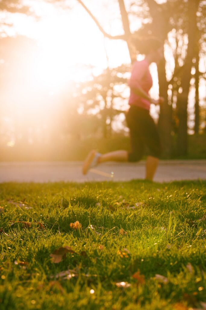 A woman jogging through a sunlit park during sunrise, embodying wellness and vitality.