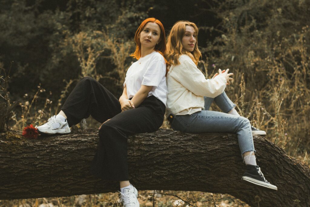 Two young women with red hair enjoying leisure time on a forest log in autumn.