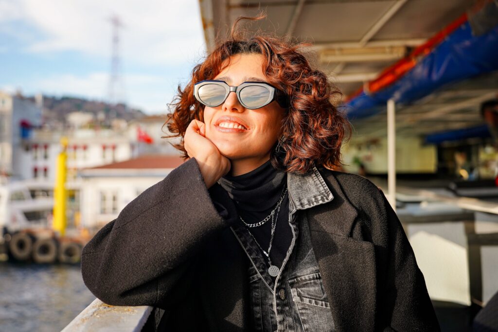 Woman enjoying a sunny day on a ferry, wearing sunglasses and a black outfit.