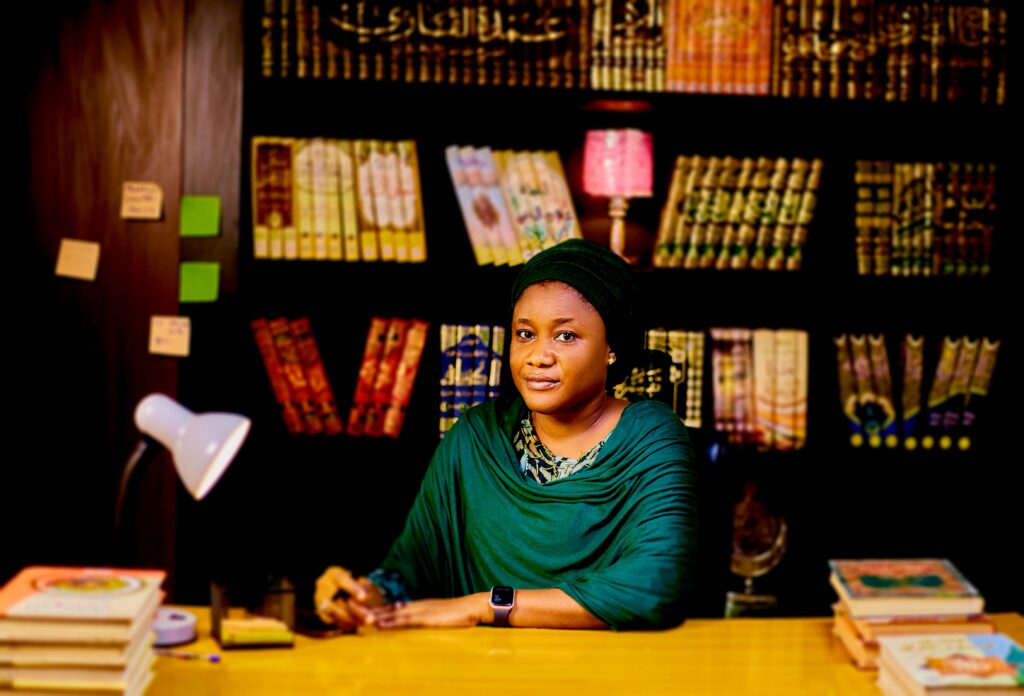 Woman in a library setting with bookshelves, conveying knowledge and professionalism.