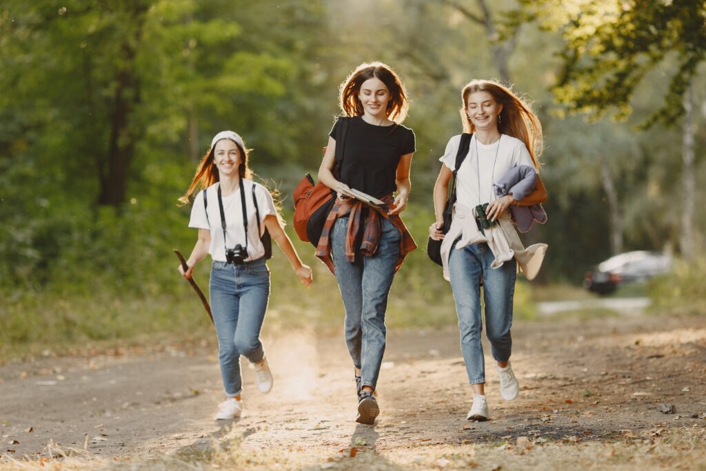 Three friends walking and smiling on a dirt road in a sunny park, enjoying the outdoors.