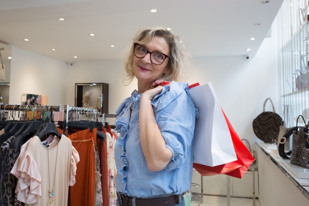Happy woman shopping with bags over shoulder in fashion boutique, enjoying retail therapy.