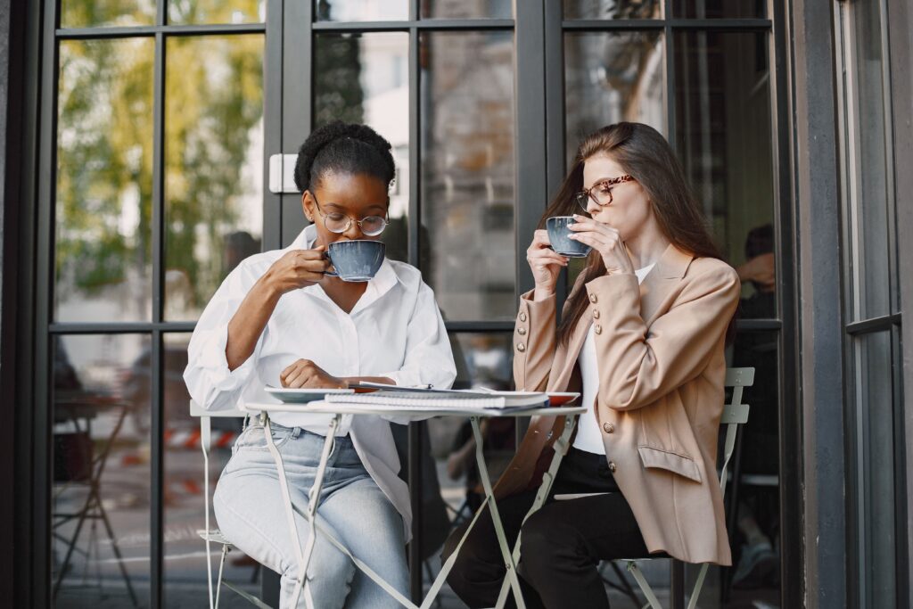 Two women enjoying coffee outdoors at a stylish cafe table.