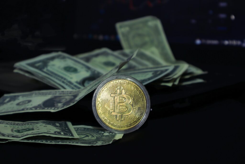 Why War Really Does Move the Bitcoin Market Bitcoin coin surrounded by scattered US dollar bills on a dark surface, symbolizing modern finance.