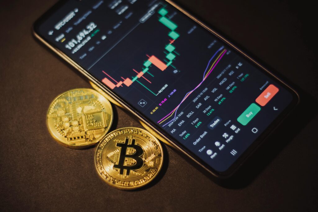 How to Buy Your First Cryptocurrency Step by Step Smartphone displaying trading app with Bitcoin coins on a dark surface.