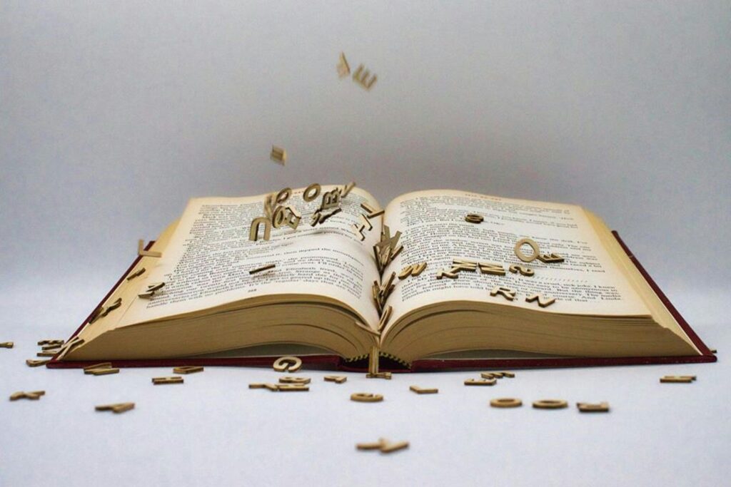Crypto Glossary: 30 Terms Every Beginner Needs to Know An open book with scattered wooden letters creating a surreal scene.