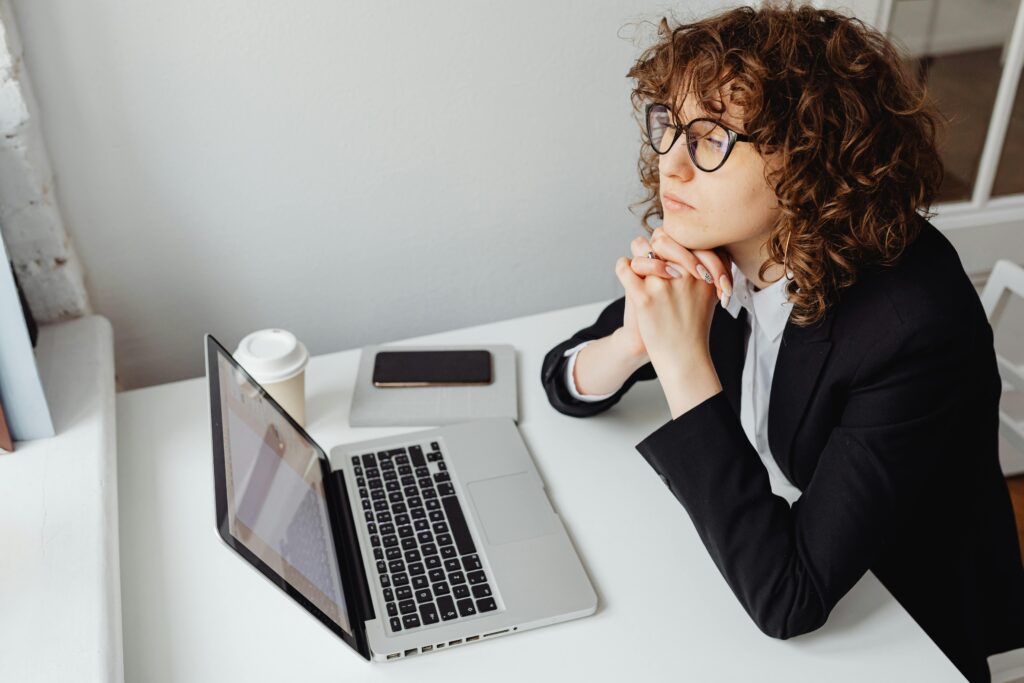 Who Should You Trust for Crypto Advice A pensive woman in business attire sits at a desk with a laptop, contemplating work.
