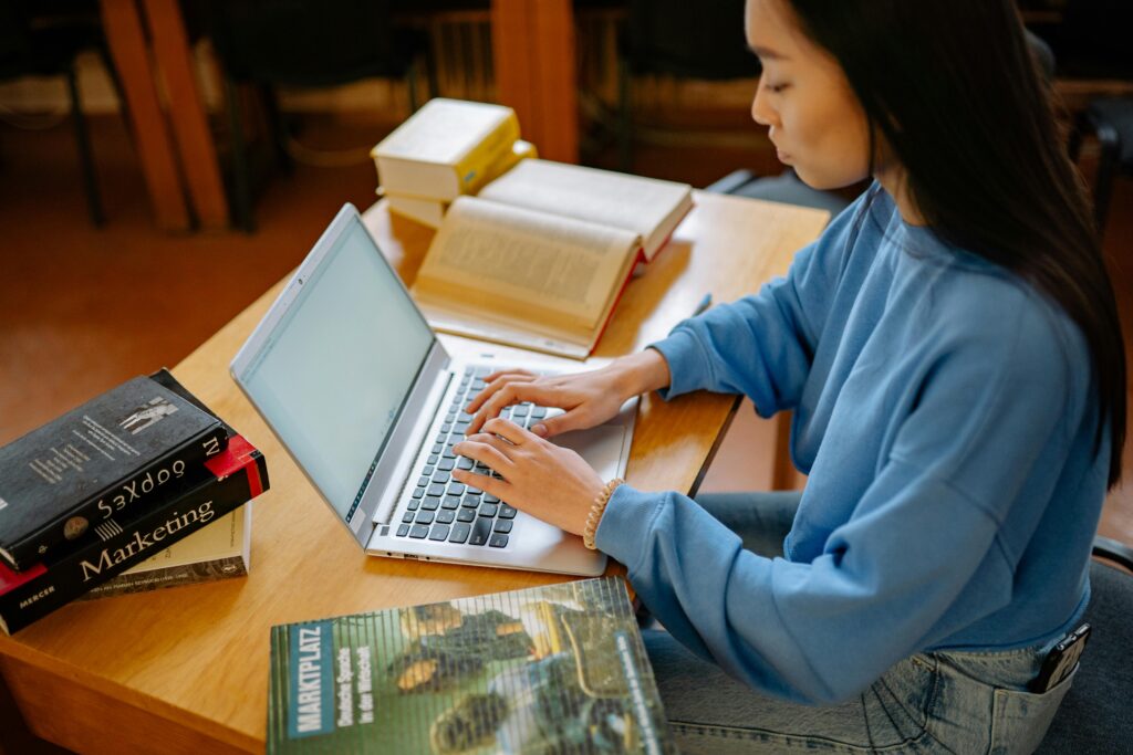 Crypto 101: Everything a Beginner Needs to Know Before They Invest Young woman typing on a laptop surrounded by textbooks in a library setting.