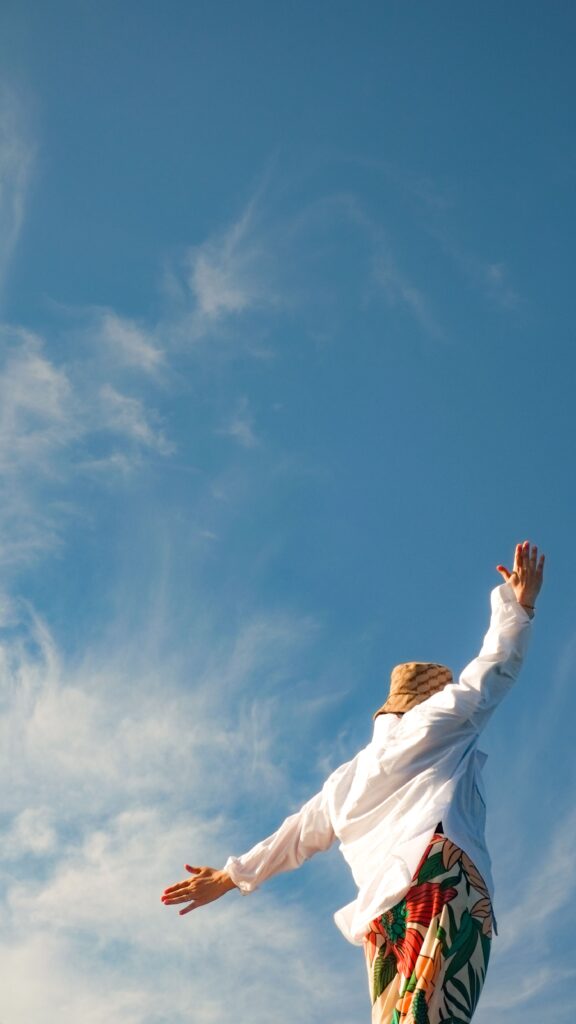 A joyful woman with arms spread wide looks to the sky, capturing the essence of freedom and summer.